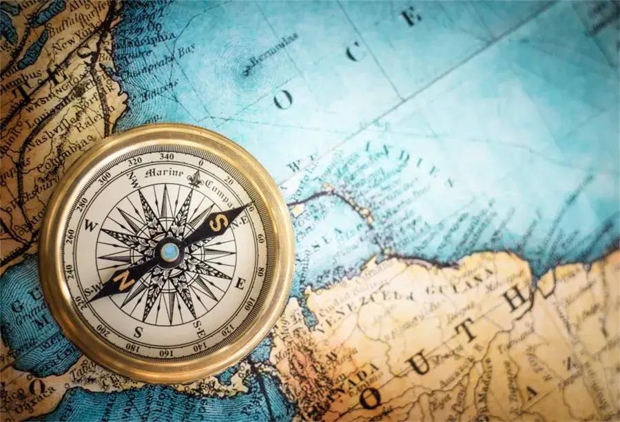 A vintage compass rests on an old, colourful map showing parts of North and South America and the Atlantic Ocean, symbolising navigation, exploration, and the importance of support coordination on every journey.